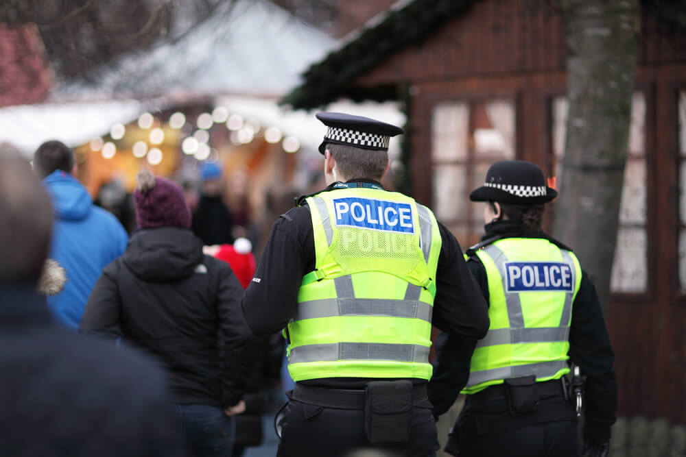 The backs of 2 police men wearing police vests.